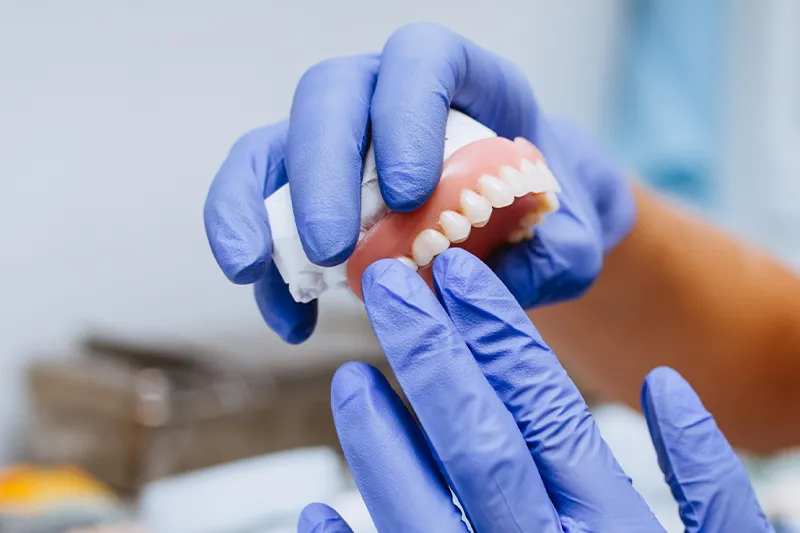 Zahnzusatz-Versicherung – Zahntechniker hält herausnehmbaren Zahnersatz in der Hand